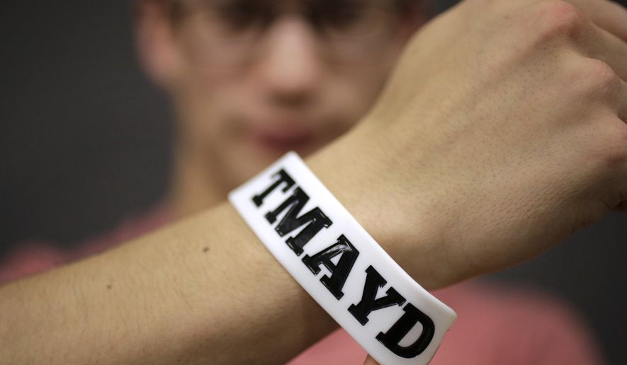 In this Monday, Feb. 1, 2016 photo, Massachusetts Institute of Technology student Andy Trattner, of Portland, Ore., displays a wrist band that features the acronym TMAYD for "Tell Me About Your Day," a campaign to encourage students to talk to one another in an effort to defuse to the stress of campus life before it leads to a crisis. There were several campus suicides last year. MIT officials recently set aside thousands of dollars for grants to help support campus projects dealing with mental health. (AP Photo/Steven Senne)