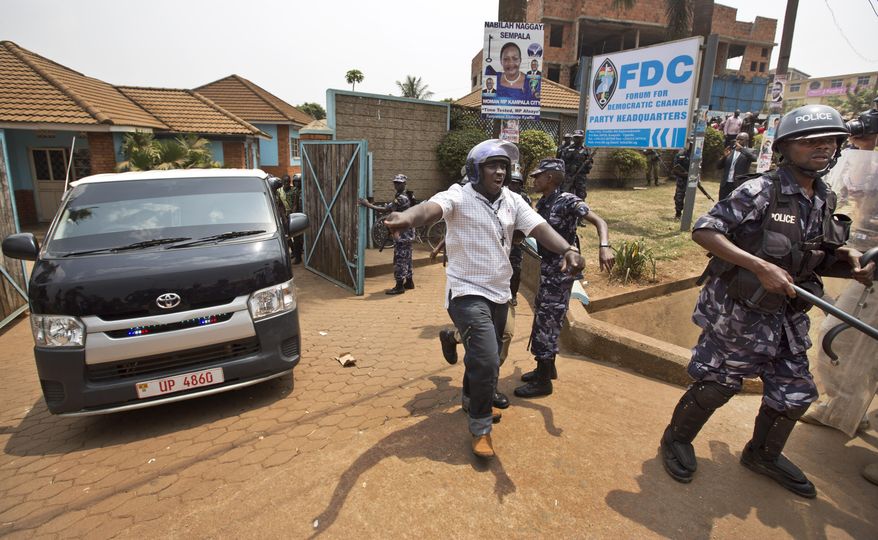 A plain-clothes policeman shouts to the media to get away as a black-windowed police van believed to contain arrested opposition leader Kizza Besigye speeds away under a police escort, at his party headquarters in Kampala, Uganda, Friday, Feb. 19, 2016. Police in Uganda arrested opposition leader Kizza Besigye at his party's headquarters Friday after heavily armed police surrounded the building and fired tear gas and stun grenades at his supporters who took to the streets. (AP Photo/Ben Curtis)