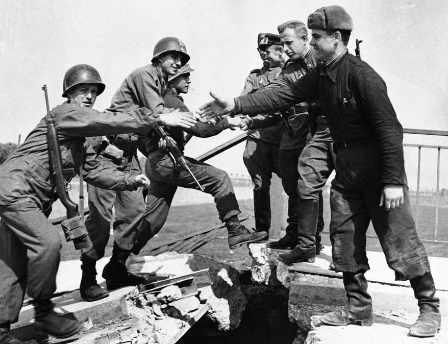 U.S. and Russian troops meet on the wrecked bridge over the Elbe River at Torgau, Germany, April 26, 1945. The Americans, left, and Russian soldiers are shown as they reach out to grasp each other&#x27;s hands. (AP Photo)