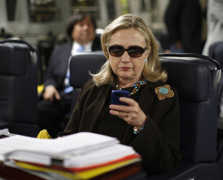 In this Oct. 18, 2011, file photo, then-Secretary of State Hillary Rodham Clinton checks her Blackberry from a desk inside a C-17 military plane upon her departure from Malta, in the Mediterranean Sea, bound for Tripoli, Libya. (AP Photo/Kevin Lamarque, Pool, File)