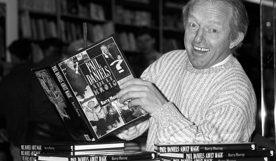 FILE - This is a Dec. 2, 1989 file photo of British magician Paul Daniels as he holds with a copy of his book 'Adult Magic' at Whiteleys book shop in London. Daniels, best known for The Paul Daniels Magic Show that regularly attracted 15 million TV viewers in Britain and was sold to 43 countries, has died after suffering from an inoperable brain tumor. He was 77. His publicist, Bex Colwell, said, in a statement that Daniels died Thursday March 17, 2016, at his home in Berkshire, 60 miles (95 kms) west of London with his wife by his side. (PA/File via AP) UNITED KINGDOM OUT