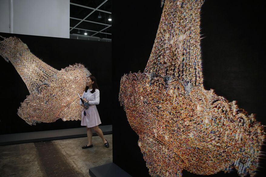 A woman walks past an artwork "Chandeliers for Five Cities" created by South Korean artist Ham Kyungah during the VIP preview of the art fair "Art Basel" in Hong Kong, Tuesday, March 22, 2016. Ham presented "Chandeliers in Five Cities," the latest in her series of embroidered works crafted with the help of unidentified North Korean workers. Ham settled on chandeliers as a reference to political power after she noticed one in a picture of world leaders meeting to divide the Korean Peninsula into north and south at the end of World War II. (AP Photo/Kin Cheung)