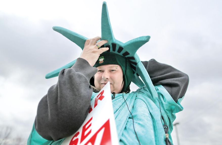 In this Wednesday, March 16, 2016 photo, Nathan Thomas places the final piece of his outfit on as he starts his shift as one of the seasonal "Statue of Liberty" wavers for Liberty Tax in Janesville, Wis. Thomas has become known by some for his singing and gestural guitar moves with the advertisement board while working. (Anthony Wahl/The Janesville Gazette via AP) MANDATORY CREDIT