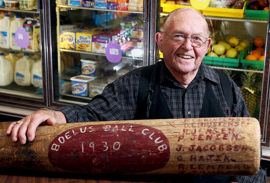 In this March 23, 2016 photo, Gene Whitefoot, who has worked at Whitefoot Market for 75 years, sits with a larger than life size 1930 Boelus Ball Club baseball bat that has several family members names on it, at the store in Boelus, Neb. (Andrew Carpenean /The Independent via AP) MANDATORY CREDIT