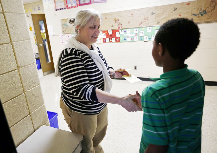 In this March 23, 2016 photo, Goshen Lane Elementary aide and etiquette teacher Mindy McFann hands out a thank-you card in exchange for a handshake from fifth grader Abinur Sileshi after teaching a small group of students about manners and etiquette during the lunch period at the Gahanna school, in Columbus, Ohio (Adam Cairns /The Columbus Dispatch via AP) MANDATORY CREDIT