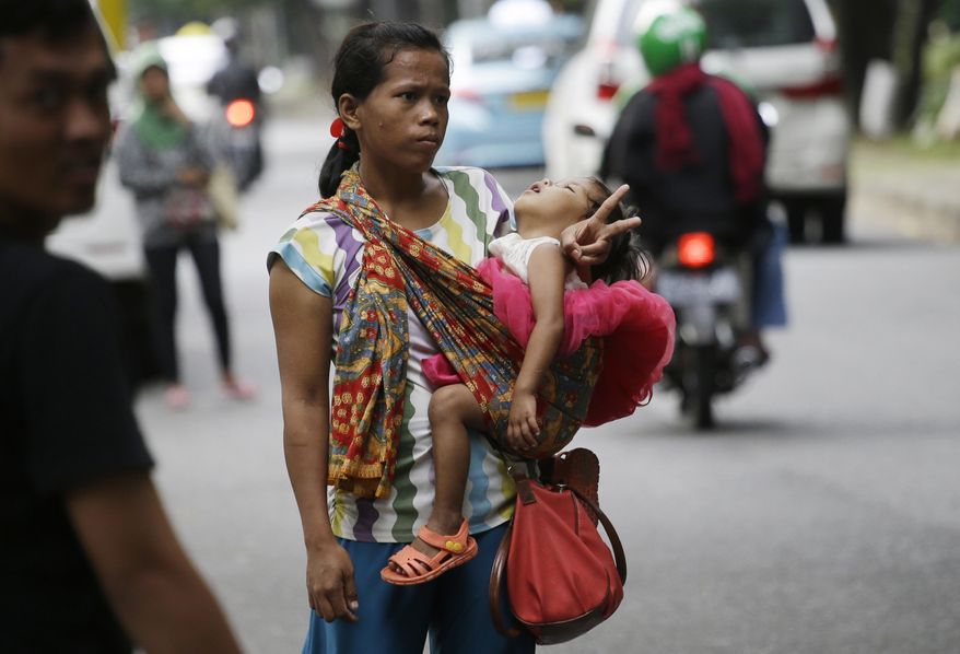 In this Friday, April 1, 2016, photo, a woman carries her baby as she signals to show that she's for hire as a "jockey" to help drivers cheat a peak time traffic rule of three people to one car during rush hour, at the main business district in Jakarta, Indonesia. Traffic clogged Jakarta planned to suspend the peak time traffic rule this week raising concerns among the jockeys that they could lose their way to eke out living. (AP Photo/Achmad Ibrahim)