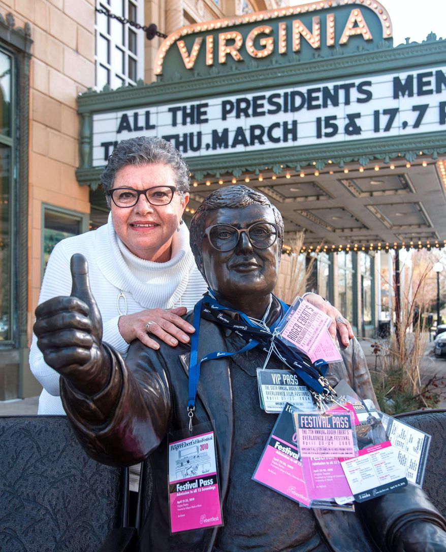 In this March 15, 2016 photo, Amani Ayad hangs all her Ebertfest passes around a statue of the late film critic outside the Virginia Theatre in Champaign, Ill. Ayad has been a hostess for Roger Ebert's Film Festival guests every year since 2003. She and the more than dozen other hosts pick up their guests and take them back to the airport and to and from their hotel and to festival events. She ferried around a festival guest in 2014 whom she had never heard of before. Two years later Ayad would see the actress, Brie Larson, pick up the Academy Award for best actress for portraying a captive mother in "Room." (John Dixon/The News-Gazette via AP ) MANDATORY CREDIT