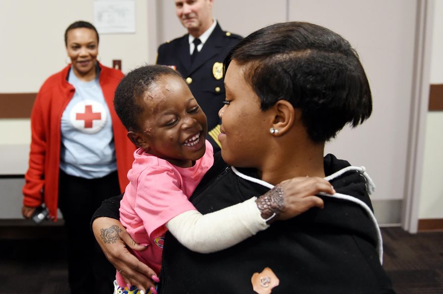 In this Tuesday, April 5, 2016 photo, two-year-old Amariyana Wells goofs around with her mother Latrice Wells in a conference room at the Van Buren Township Public Safety Department, in Mich. Firefighter John Henderson, along with several other emergency personnel, were honored for saving Amariyana from a house fire in December 2015. Henderson entered the burning structure without his helmet and later drove the ambulance to the hospital so that both paramedics could work with Amariyana in the back. The Van Buren Township Public Safety Department awarded Henderson the medal of honor, the highest honor they can bestow. (Melanie Maxwell/The Ann Arbor News via AP) LOCAL TELEVISION OUT; LOCAL INTERNET OUT; MANDATORY CREDIT