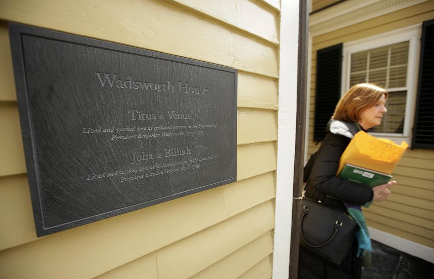 A passer-by walks near a newly unveiled plaque attached to Wadsworth House, Wednesday, April 6, 2016, on the campus of Harvard University that honors four slaves that had been owned by and worked for Harvard's past presidents, in Cambridge, Mass. (AP Photo/Steven Senne)