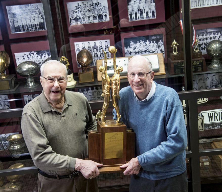 In this March 15, 2016 photo, Earl Harrison, left, and Ted Beach, members of the 1946 Champaign High School basketball team, hold the championship trophy they won, in front of the trophy case at Champaign Central High School, in Champaign, Ill. "I don't remember if I touched it when we won it," Harrison said. "I know if I did, this is the first time I've touched it since then." (John Dixon/The News-Gazette via AP) MANDATORY CREDIT