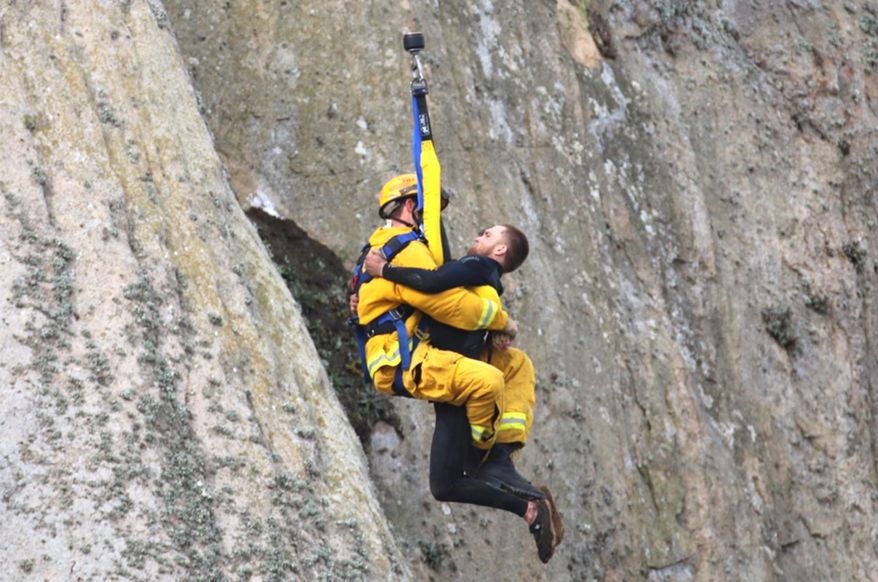In this photo provided by Bob Isenberg, Michael Banks is rescued after being stranded on a ledge some 80 off the ground on Morro Rock, a landmark in Morro Bay, Calif., Thursday, April 7, 2016. He had scaled the rock to make an Internet proposal to his girlfriend - who said yes - but then got stuck on a ledge and couldn't get down. A helicopter had to be called, and Morro Bay Fire Department Capt. Todd Gailey was lowered by cable to pluck Banks and take him to safety.(Bob Isenberg via AP)