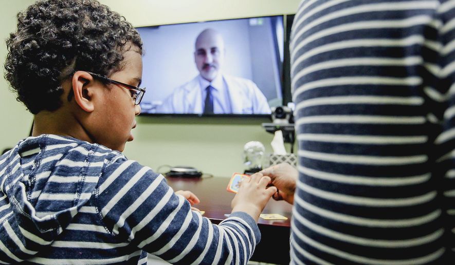 In this March 14, 2016 photo, Evan Crudup, 4, of Algonquin, Ill., plays with his father during his appointment with Dr. Marvin Rossi via telehealth video conferencing in Crystal Lake, Ill. Rossi, a neurologist at Rush University Medical Center in Chicago, is able to connect with his patients in McHenry County using a form of telehealth the Epilepsy Foundation has been using for about two years. (Sarah Nader/Northwest Herald via AP) MANDATORY CREDIT; CHICAGO TRIBUNE OUT