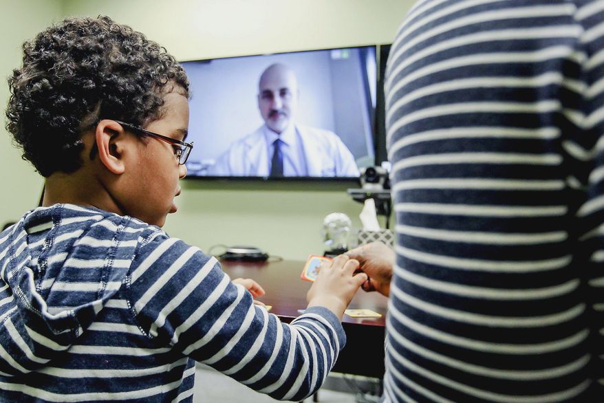 In this March 14, 2016 photo, Evan Crudup, 4, of Algonquin, Ill., plays with his father during his appointment with Dr. Marvin Rossi via telehealth video conferencing in Crystal Lake, Ill. Rossi, a neurologist at Rush University Medical Center in Chicago, is able to connect with his patients in McHenry County using a form of telehealth the Epilepsy Foundation has been using for about two years. (Sarah Nader/Northwest Herald via AP) MANDATORY CREDIT; CHICAGO TRIBUNE OUT