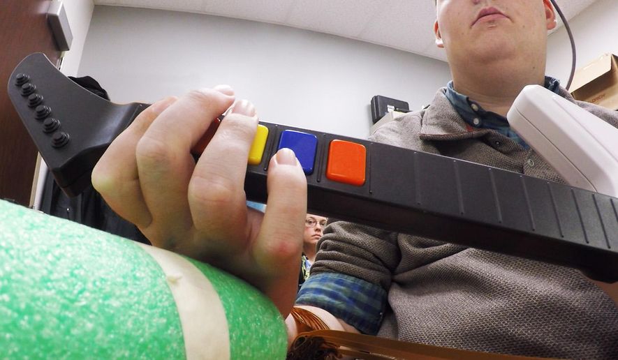In this March 2016 photo provided by Ohio State University, Ian Burkhart plays a guitar video game as part of a study with neural bypass technology at The Ohio State University Wexner Medical Center in Columbus. A computer chip in Burkhart's brain reads his thoughts, decodes them, then sends signals to a sleeve on his arm, that allows him to move his hand. (Clark Powell/Ohio State University Wexner Medical Center via AP)