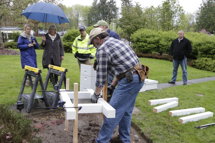 Members of the Olympia Beekeepers Association install a base for bee hive boxes on the front lawn of the governor's mansion as first lady Trudi Inslee, holding umbrella, looks on, in Olympia, Wash., Thursday, April 14, 2016. About 30,000 European honeybees will be placed in the hives next week as part of an effort to raise awareness about the decline of bee populations, as well as to boost pollination of plants on the Capitol campus. (AP Photo/Rachel La Corte)