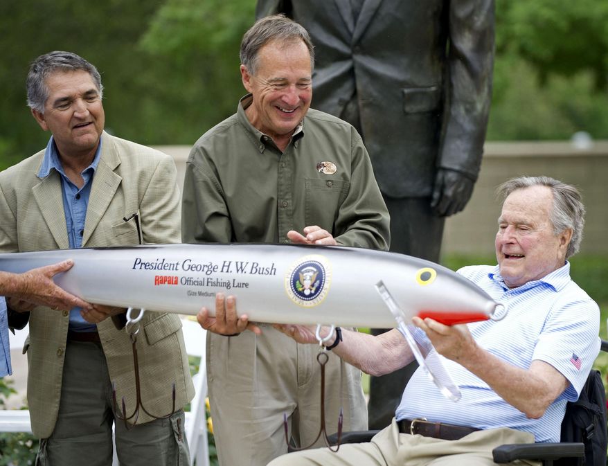 In this April 14, 2016 photo, Bass Pro Shops founder Johnny Morris, center, joins Pedro Sors, president of the fishing association of the Mexican state of Tamaulipas, as they present former president George H.W. Bush with a giant-sized fishing lure at the Bush Library in College Station, Texas. (Dave McDermand/College Station Eagle via AP) MANDATORY CREDIT