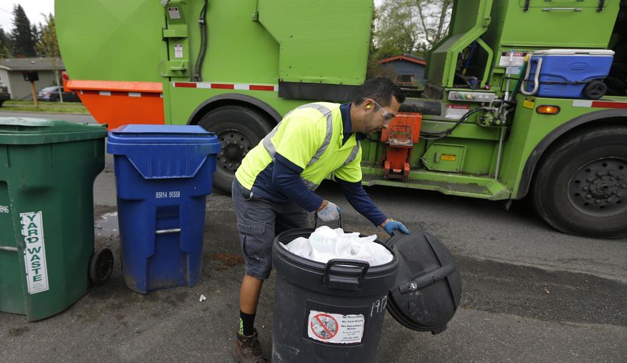 David Morales, a garbage driver with Recology, picks up a garbage container for Seattle Public Utilities, Friday, April 15, 2016, in Seattle. A judge is scheduled to hear a challenge Friday, April 16, 2016, to a new Seattle law allowing garbage collectors to check people's trash to see whether they are disposing of recycling items and food waste incorrectly. (AP Photo/Ted S. Warren)