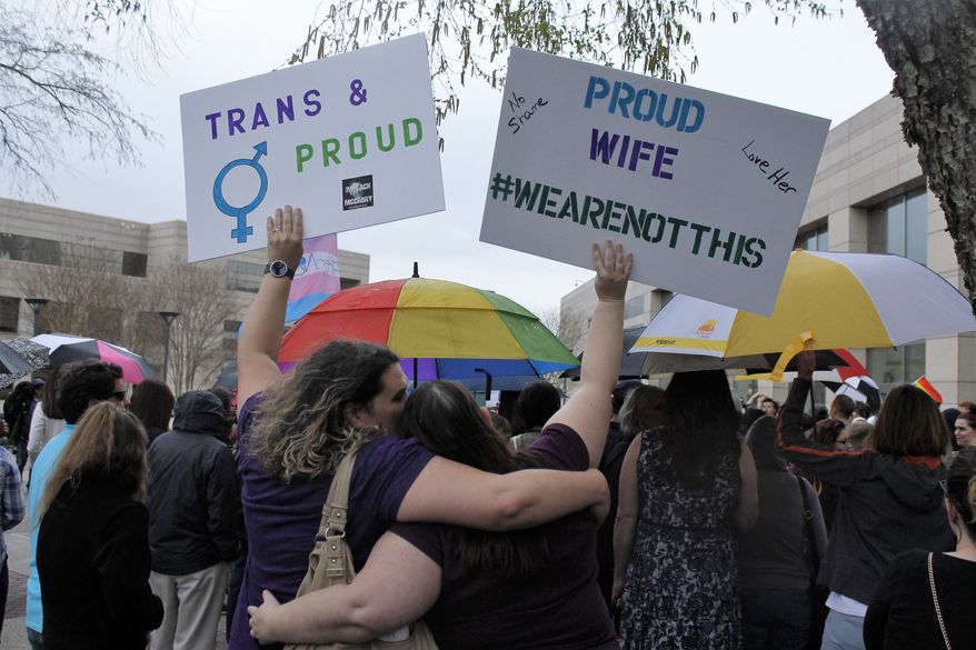 Two protesters hold up signs against passage of legislation in North Carolina, which limits the bathroom options for transgender people, during a rally in Charlotte, N.C., Thursday, March 31, 2016. The rally drew around 100 people at the Charlotte-Mecklenburg Government Center. (AP Photos/Skip Foreman)