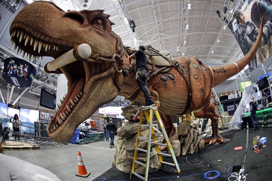 Joshua Patino stands on a ladder to put finishing touches on a giant dinosaur exhibit at PAX East in the Boston Convention and Expo Center, Thursday, April 21, 2016, in Boston. PAX East, an annual celebration of gaming culture, is expected to draw tens of thousands of visitors Friday through Sunday. It's a place where serious gamers can preview unreleased video games and devices, compete in tournaments, hear live music and meet others for whom gaming is a way of life. (AP Photo/Elise Amendola)
