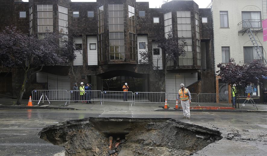 A San Francisco Public Utilities Commission worker stands over a large sinkhole on Sacramento Street in San Francisco, Friday, April 22, 2016. According to a spokesperson for the the city's Public Utilities Commission, the sinkhole appeared on Thursday, caused by a broken sewer pipe line. (AP Photo/Jeff Chiu)