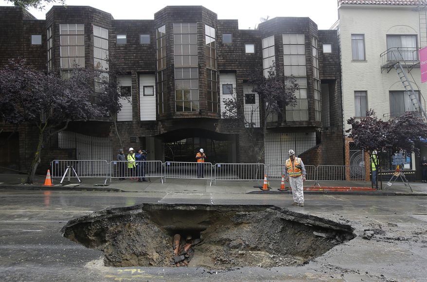 A San Francisco Public Utilities Commission worker stands over a large sinkhole on Sacramento Street in San Francisco, Friday, April 22, 2016. According to a spokesperson for the the city's Public Utilities Commission, the sinkhole appeared on Thursday, caused by a broken sewer pipe line. (AP Photo/Jeff Chiu)