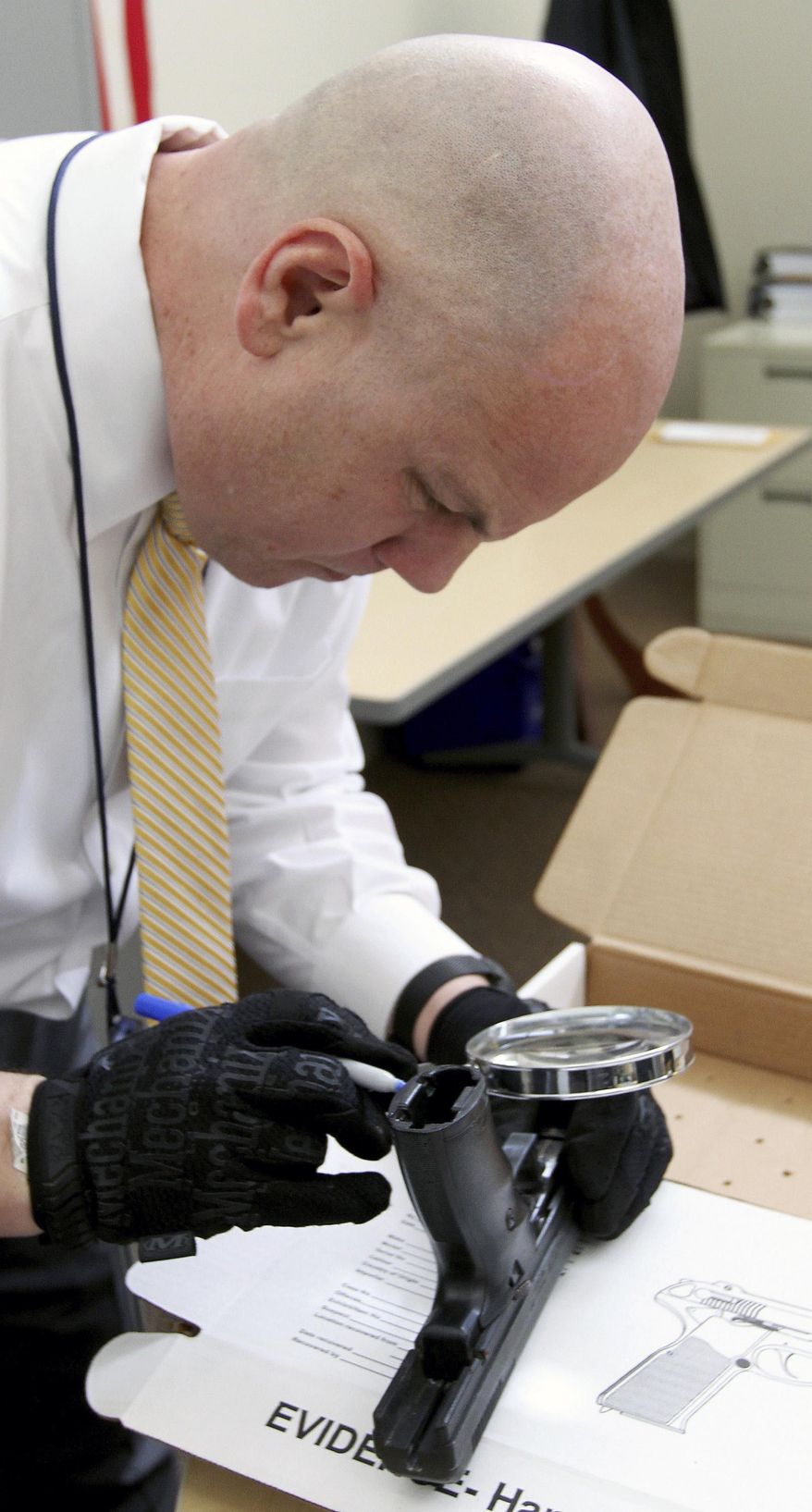 ADVANCE FOR WEEKEND EDITIONS APRIL 23-24 - In this Thursday, April 4, 2016 photo, Corp. Brian Morel, an ATF Task Force officer, uses a magnifying glass to read this gun's serial number at his desk in the Davenport Police station in Davenport, Iowa. Morel then can input it into the National Tracing Center, the ATF's online database that lists all guns sold through a licensed federal firearms dealer. While the database cannot tell officers whether the gun was reported stolen, the information obtained can serve as a jumping-off point for investigators as they try to track down its origin. (John Schultz/Quad City Times via AP) MANDATORY CREDIT