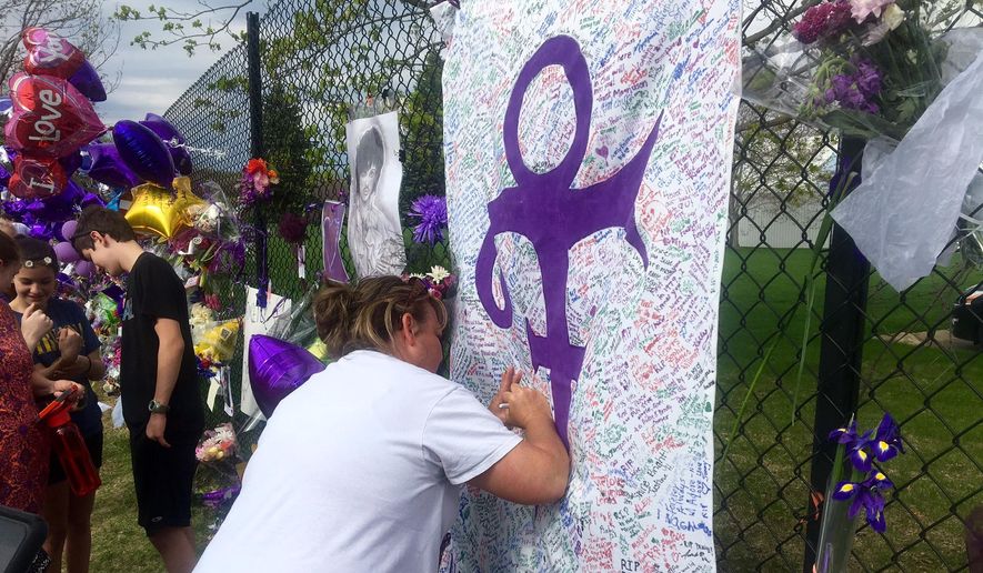 A woman writes on memorial sheet adorned with the symbol Prince once used to identify himself outside Paisley Park in Chanhassen, Minn., Saturday, April 23, 2016. The music superstar was pronounced dead at his Paisley Park estate near Minneapolis on Thursday. He was 57. (AP Photo/Jeff Baenen)