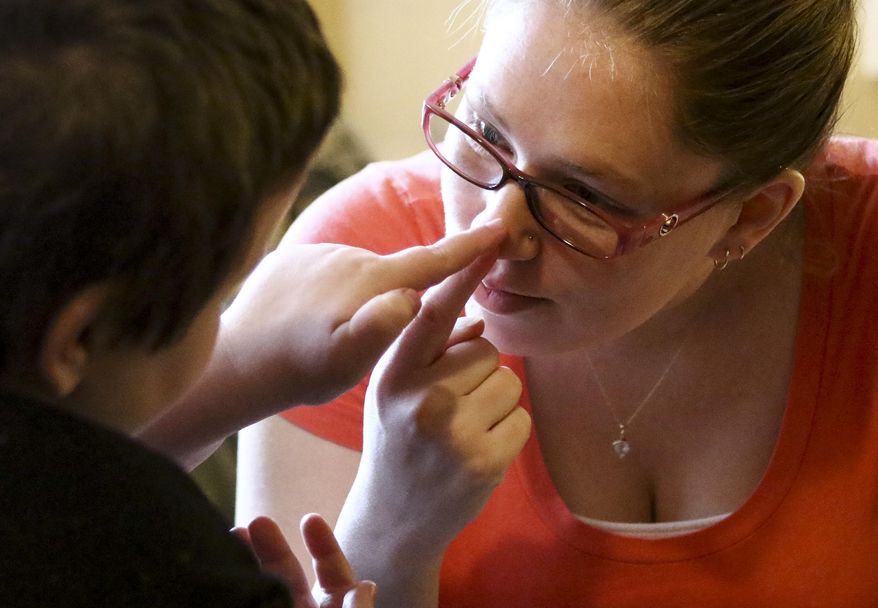 In this undated photo, Andrea Cales, occupational therapist with Applied Behavior Analysis, asks Jessie Pyles to point her nose in Lake Stevens, Wash. Jessie, who has autism with developmental delay, a sensory-processing disorder and other medical conditions, cannot speak but according to The Daily Herald he loves words. (Kevin Clark/The Daily Herald via AP) MANDATORY CREDIT