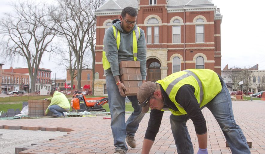 In a Tuesday, April 19, 2016 photo, Ryan Parlove places bricks in the Historic Livingston County Courthouse amphiteater while Chris Juarez keeps the supply coming and Cody Watkins unloads a new pallet of bricks. The Evergreen Outdoor employees will install over 36,000 bricks between the upper area they work on here and the lower area closer to Grand River by the time the job is complete. (Gillis Benedict/Livingston Daily Press & Argus via AP)