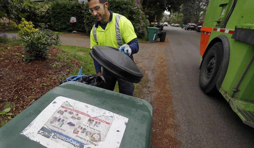 FILE - In this April 15, 2016 file photo, David Morales, a garbage driver with Recology, picks up a garbage container for Seattle Public Utilities in Seattle. A judge on Wednesday, April 27, 2016 stopped enforcement of a Seattle ordinance barring people from throwing compost in the trash, declaring it unconstitutional. The measure required trash collectors to tag garbage cans that contain more than 10 percent compostable material with education information. (AP Photo/Ted S. Warren, File)
