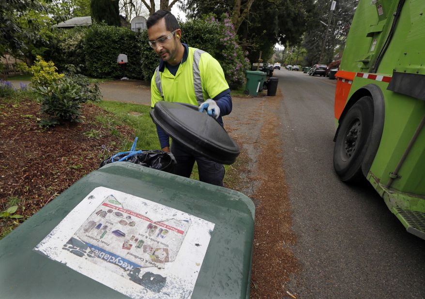 FILE - In this April 15, 2016 file photo, David Morales, a garbage driver with Recology, picks up a garbage container for Seattle Public Utilities in Seattle. A judge on Wednesday, April 27, 2016 stopped enforcement of a Seattle ordinance barring people from throwing compost in the trash, declaring it unconstitutional. The measure required trash collectors to tag garbage cans that contain more than 10 percent compostable material with education information. (AP Photo/Ted S. Warren, File)