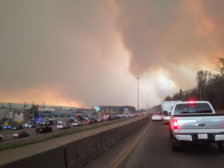 Smoke from a wildfire rises in the air as cars line up on a road in Fort McMurray, Alberta, Tuesday, May 3, 2016. At least half of a northern Alberta city was ordered evacuated Tuesday as a wildfire whipped by winds engulfed homes and sent ash raining down on residents. (Greg Halinda/The Canadian Press via AP) MANDATORY CREDIT