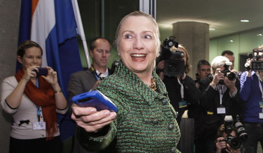 In this Dec. 8, 2011, file-pool photo, then-Secretary of State Hillary Rodham Clinton hands off her mobile phone after arriving for a meeting in The Hague, Netherlands. (AP Photo/J. Scott Applewhite, Pool, File)