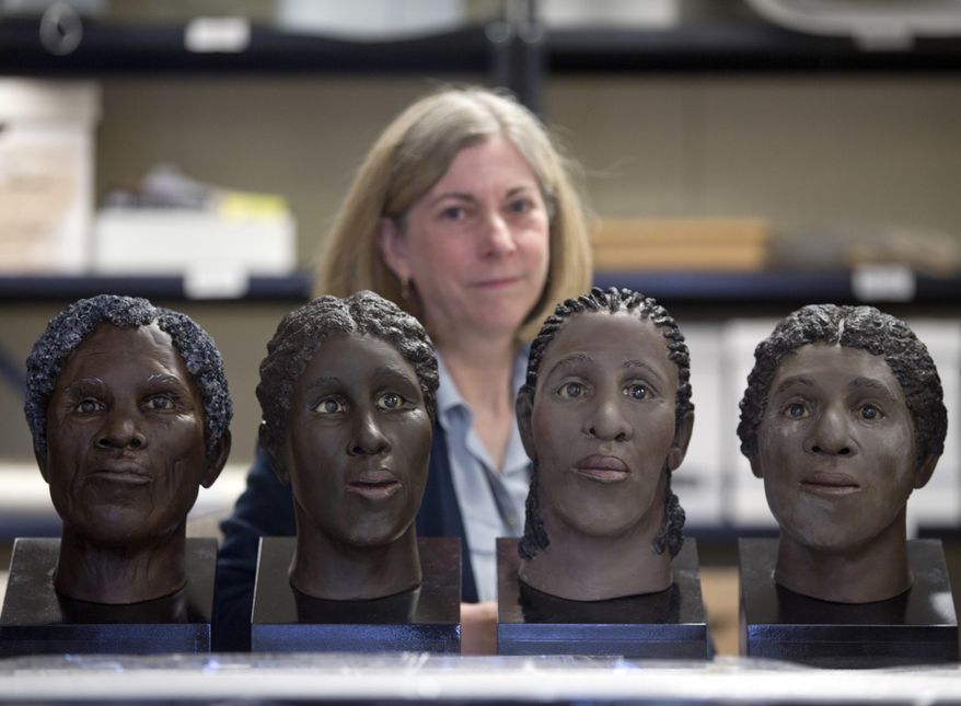 In this April 27, 2016 photo, Lisa Anderson, curator of bioarchaeology at the New York State Museum, poses in Albany, N.Y., with facial reconstructions of slaves found at an unmarked cemetery. The reconstructions were done by the museum. Fourteen slaves will be buried a second time, a decade after construction workers accidentally uncovered their remains north of Albany. (AP Photo/Mike Groll)