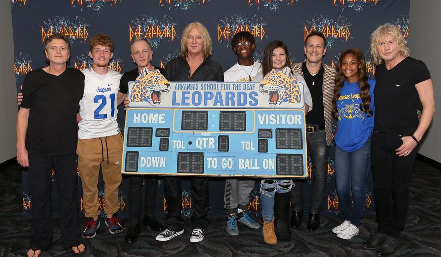CORRECTS DATE TO MAY 11 - In this May 11, 2016 photo provided by Nelson Chenault, from left, Def Leppard drummer Rick Allen, student Stephen Cathcart, guitarist Phil Collen, lead singer Joe Elliott, student Henry James, student Alex Gossett, guitarist Vivian Campbell, student Jewel Brandon and bassist Rick Savage pose with a replica of the scoreboard from the Arkansas School for the Deaf, before a concert in North Little Rock, Ark. The British rockers behind a string of hits in the 1980s and '90s including "Pour Some Sugar on Me" and "Photograph" met with students whose team's name is the Leopards. (Nelson Chenault via AP)