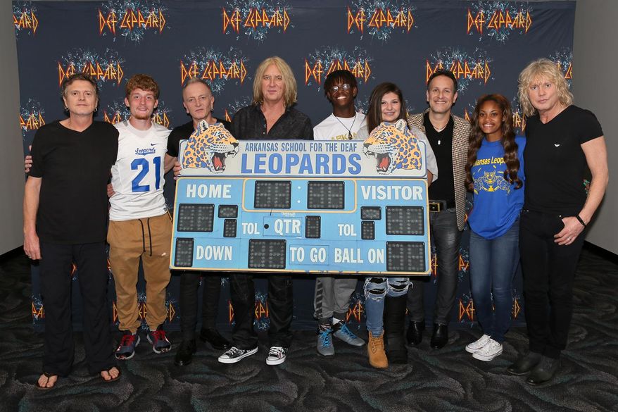 CORRECTS DATE TO MAY 11 - In this May 11, 2016 photo provided by Nelson Chenault, from left, Def Leppard drummer Rick Allen, student Stephen Cathcart, guitarist Phil Collen, lead singer Joe Elliott, student Henry James, student Alex Gossett, guitarist Vivian Campbell, student Jewel Brandon and bassist Rick Savage pose with a replica of the scoreboard from the Arkansas School for the Deaf, before a concert in North Little Rock, Ark. The British rockers behind a string of hits in the 1980s and '90s including "Pour Some Sugar on Me" and "Photograph" met with students whose team's name is the Leopards. (Nelson Chenault via AP)