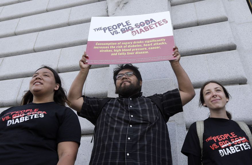 Jesus Alonso, center, holds up a sign between other volunteers after a news conference announcing that San Francisco backers of a tax on sugary beverages have enough signatures to put the measure on the November ballot outside of City Hall in San Francisco, Thursday, May 12, 2016. This would be San Francisco's second attempt in two years trying to put a tax on the highly caloric drinks that some public health advocates say contributes to obesity. A 2014 attempt failed to garner the two-thirds approval needed for a dedicated tax. (AP Photo/Jeff Chiu)