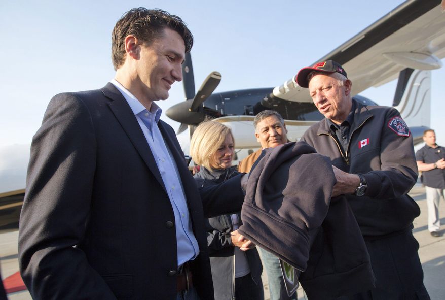 Canada Prime Minister Justin Trudeau is presented with a jacket from Fort McMurray fire chief Darby Allen in Edmonton, Friday, May 13, 2016, before a flight to Fort McMurray. Trudeau is making the visit to see first-hand the devastation caused by the wildfire that forced the evacuation of the city. (Jason Franson/The Canadian Press via AP) MANDATORY CREDIT