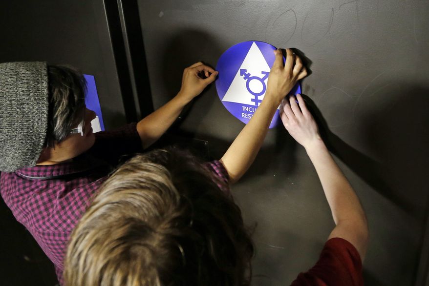 Destin Cramer, left, and Noah Rice place a new sticker on the door at the ceremonial opening of a gender neutral bathroom at Nathan Hale high school Tuesday, May 17, 2016, in Seattle. President Obama’s directive ordering schools to accommodate transgender students has been controversial in some places but since 2012 Seattle has mandated that transgender students be able to use of the bathrooms and locker rooms of their choice. Nearly half of the district’s 15 high schools already have gender neutral bathrooms and one high school has had a transgender bathroom for 20 years. (AP Photo/Elaine Thompson)