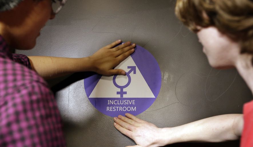 Destin Cramer, left, and Noah Rice place a new sticker on the door at the ceremonial opening of a gender neutral bathroom at Nathan Hale High School May 17 in Seattle. (Associated Press) **FILE**