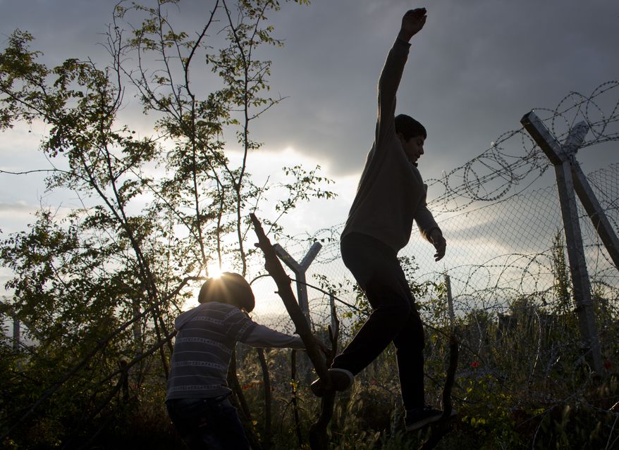 Amir (right) and Mohammed, refugees from Syria, play in front of a barbed-wire fence on the Macedonian border, in Idomeni, Greece, on May 19, 2016. Thousands of stranded refugees and migrants have camped in Idomeni for months after the border was closed. (Associated Press) **FILE**