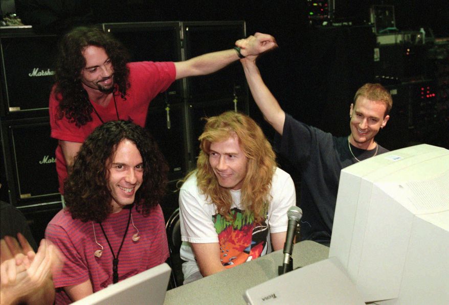In this July 24, 1997, file photo, lead guitarist Marty Friedman, left, and lead singer/guitarist Dave Mustaine, center, field questions while bassist David Ellefson, right, high-fives drummer Nick Menza, back left, during a live chat on the internet held at The Joint inside the Hard Rock hotel-casino in Las Vegas. (Ethan Miller/Las Vegas Sun via AP)