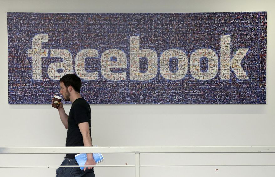 A Facebook employee walks past a sign at Facebook headquarters in Menlo Park, Calif. (Associated Press)