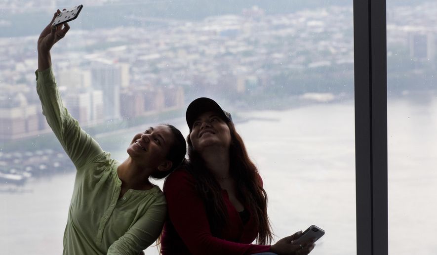 A woman takes a photo with a view of New Jersey from One World Observatory, Tuesday, May 24, 2016, in New York. It's been a year since the observatory at One World Trade Center opened to the public. (AP Photo/Mark Lennihan)