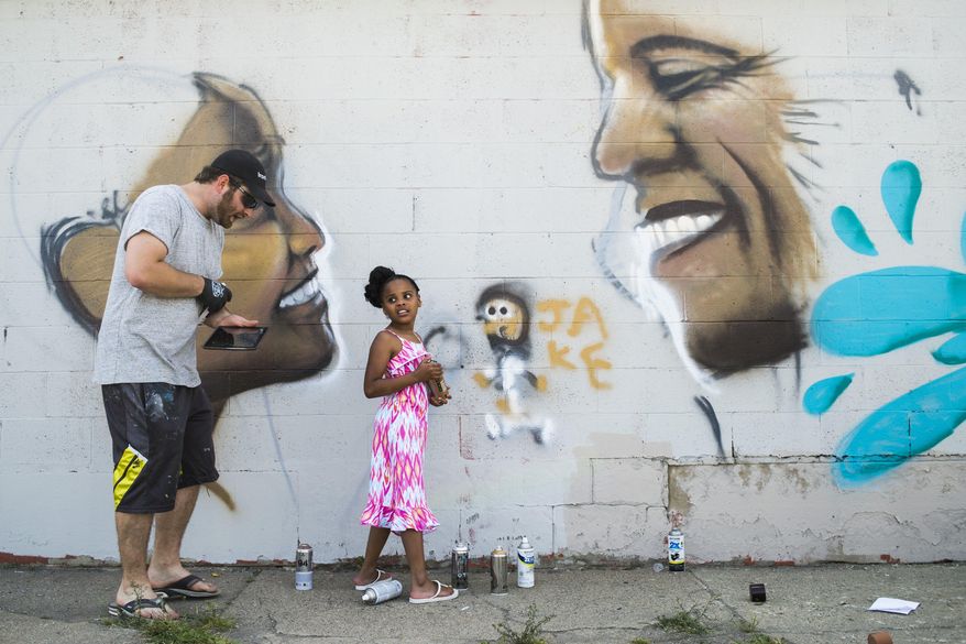 Mari "Little Miss Flint" Copeny, 8, looks back as she paints Flint Journal photojournalist Jake May onto the mural while getting tips from Flint native and street artist Kevin Burdick while he paints her likeness for a Gallery on the Go installation related to the Flint water crisis on Tuesday, May 24, 2016 at the former Union Print building, which has stood abandoned after a fire for several years at the intersection of Harriet and Saginaw Streets north of downtown Flint. (Jake May/The Flint Journal-MLive.com via AP)