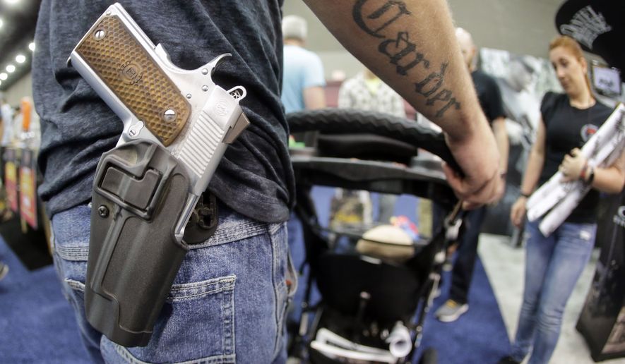 A man wears his handgun in a holster as he pushes his son in a stroller at the National Rifle Association Convention in 2016. (Associated Press)
