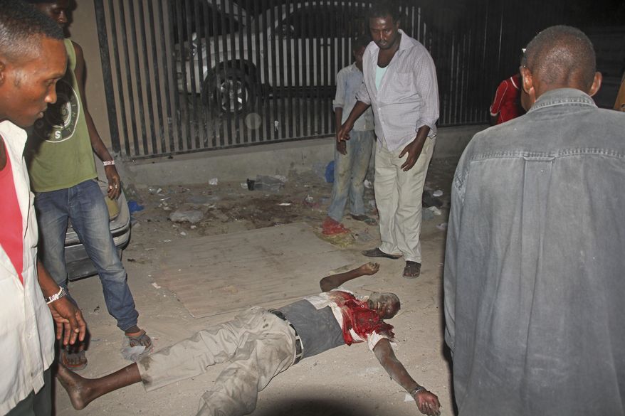 Somali men gather around a dead civilian who was killed in a bomb attack on an hotel in Mogadishu, Somalia Wednesday, June 1, 2016. The attack took place on the Ambassador hotel, which is often frequented by government officials and business executives. (AP Photo/Farah Abdi Warsameh)