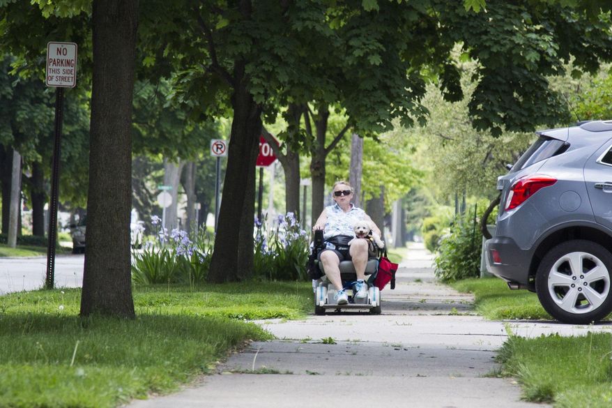 Katherine Thane makes her way the sreet with her dog Friday May 27, 2016, in Bay City, Mich. Bay City officials are proposing a fee on tax bills that would free up money to improve sidewalks citywide. (Gavin McIntyre/The Bay City Times via AP) LOCAL TELEVISION OUT; LOCAL INTERNET OUT; MANDATORY CREDIT