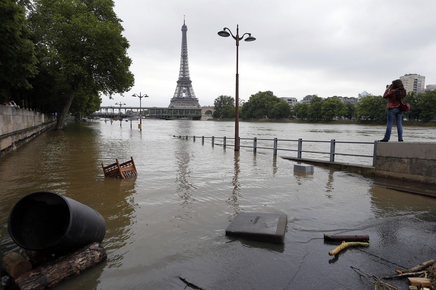 In this June 4, 2016, file photo, a woman, at right, takes photos of the flooded banks of the Seine river in Paris. An international team of scientists has found that man-made climate change nearly doubled the likelihood of last month&#39;s devastating French flooding. In a quick but not peer-reviewed analysis, the World Weather Attribution team of climate scientists used past rainfall data and computer simulations to look for global warming&#39;s fingerprints in the heavy downpours in France and Germany. (AP Photo/Francois Mori)