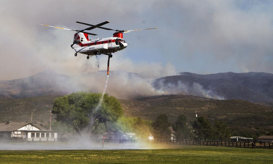 A rainbow forms as a helicopter picks up water to drop on the Tenderfoot Fire near Peeples Valley, Ariz., Thursday, June 9, 2016. A brush fire that began Wednesday pushed evacuations to several hundred as more people fled homes Thursday near Yarnell, an Arizona community. Authorities ordered additional evacuations Thursday, including homes in the Peeples Valley Area, as they feared the fire might make its way down to Highway 89. (Tom Tingle/The Arizona Republic via AP) MARICOPA COUNTY OUT; MAGS OUT; NO SALES; MANDATORY CREDIT